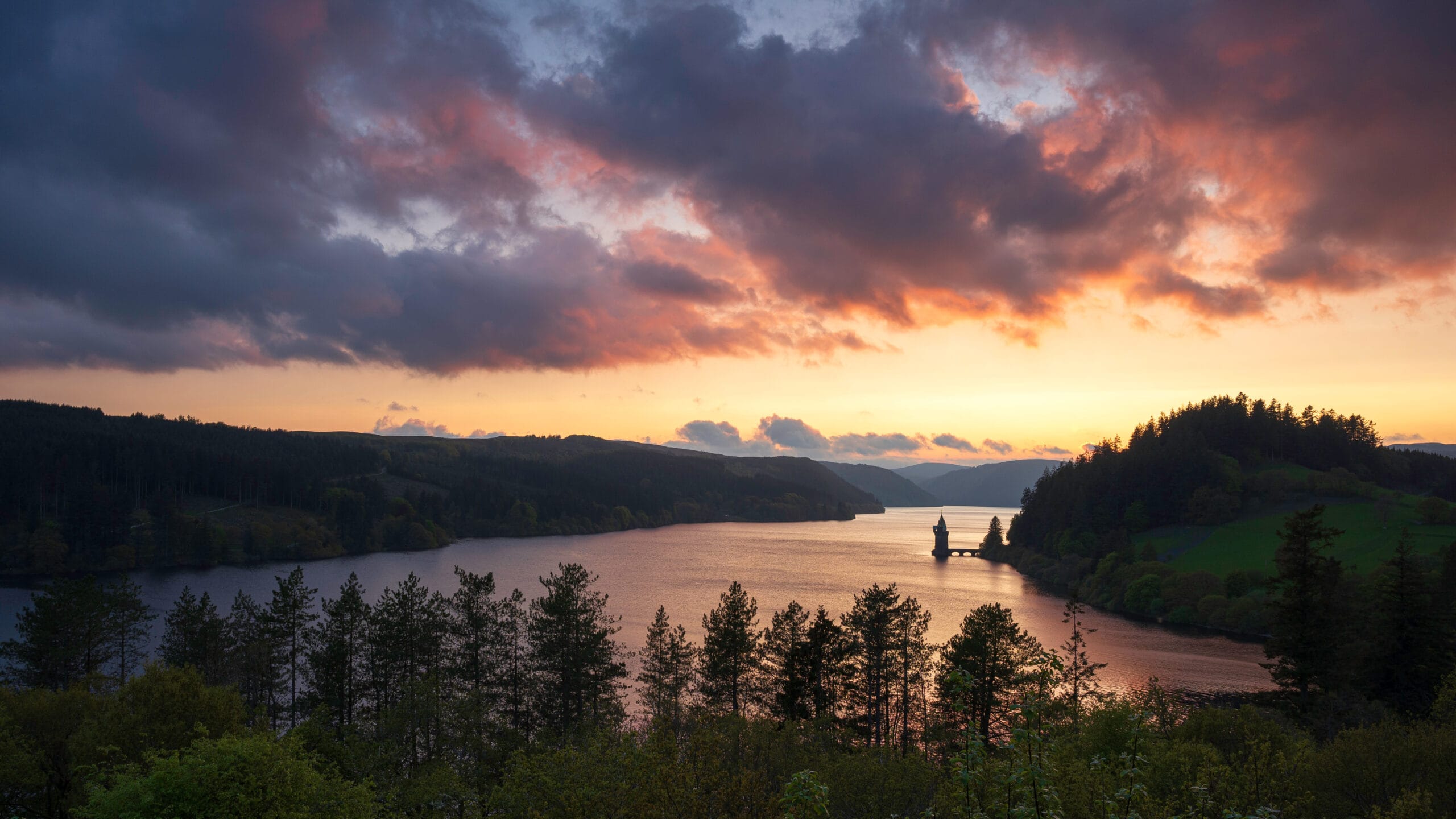 Lake Vyrnwy, located in mid Wales near Roomination Escape Rooms, an area of outstanding natural beauty, at sunset. The orange sky is reflected in the calm water of the lake